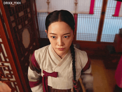 a woman in a traditional korean dress stands in front of a window with drxx_yxh written in the corner