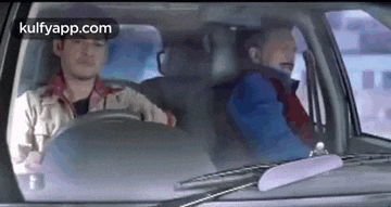 two men are sitting in a car and one of them is sleeping .