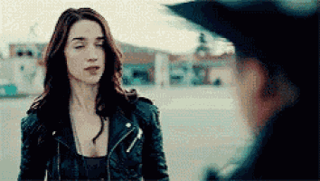 a woman in a leather jacket is standing in front of a man in a hat .