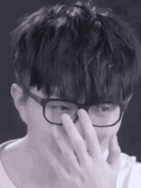 a close up of a person wearing glasses and covering their face with their hand .