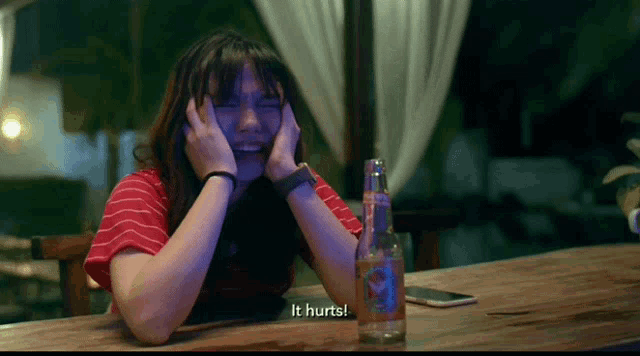 a woman sits at a table with a bottle of soda and the words it hurts behind her