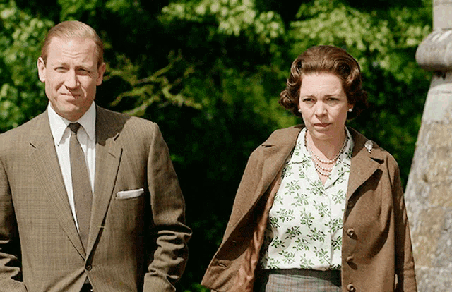 a man in a suit and tie stands next to a woman wearing a floral shirt