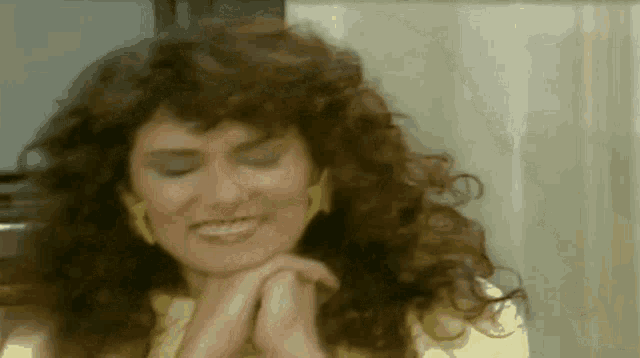 a woman with curly hair is smiling with her hand on her chin .
