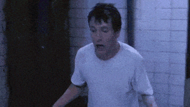 a man in a white t-shirt is standing in a bathroom with his mouth open .