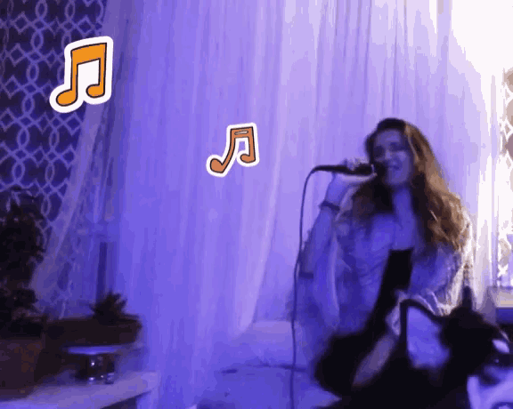 a woman singing into a microphone with a purple curtain behind her