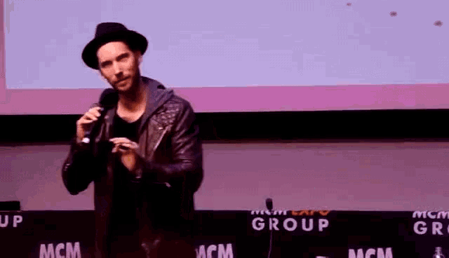 a man stands in front of a microphone in front of a mcm group sign