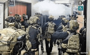 a group of soldiers are standing in a hallway with smoke coming out of a doorway .