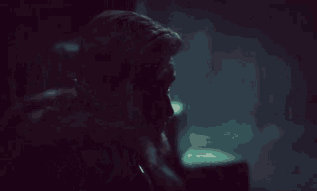 a man with a beard is sitting in a dark room with his head down .
