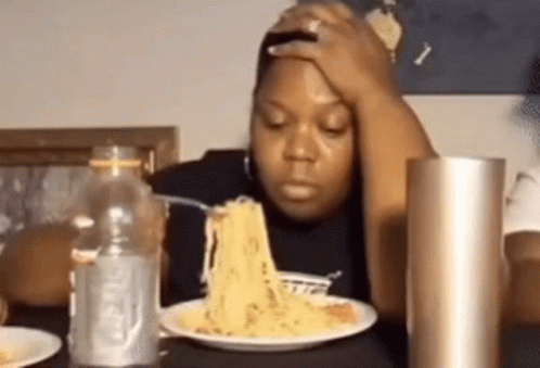 a woman is sitting at a table eating spaghetti with a fork and a bottle of water .