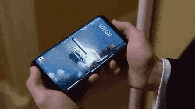 a person is holding a cell phone in their hands with a picture of a space shuttle launch on the screen .
