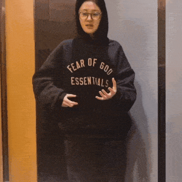 a woman wearing a fear of god essentials hoodie