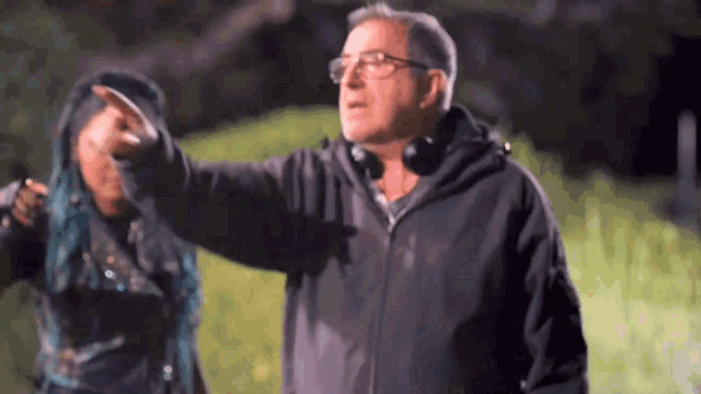 a man wearing glasses and headphones is pointing at a woman with blue hair