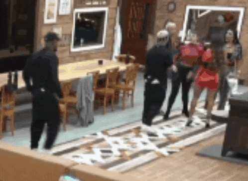a group of people are standing in a living room in front of a table and chairs .