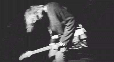 a black and white photo of a man playing a guitar while laying on the ground .