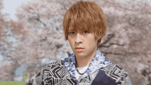 a young man wearing a floral shirt stands in front of cherry blossoms