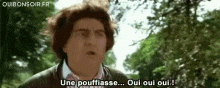 a man with curly hair is standing in front of trees and says une pouffiasse oui oui oui .