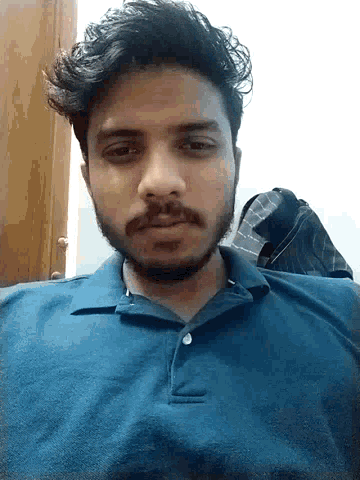 a man with a beard and a blue shirt looks at the camera