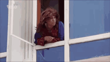 a woman in a wig is looking out a window