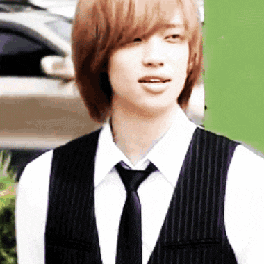 a young man wearing a vest and tie stands in front of a green wall