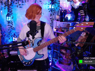 a woman is playing a blue guitar in front of a microphone with cox cam written on the screen