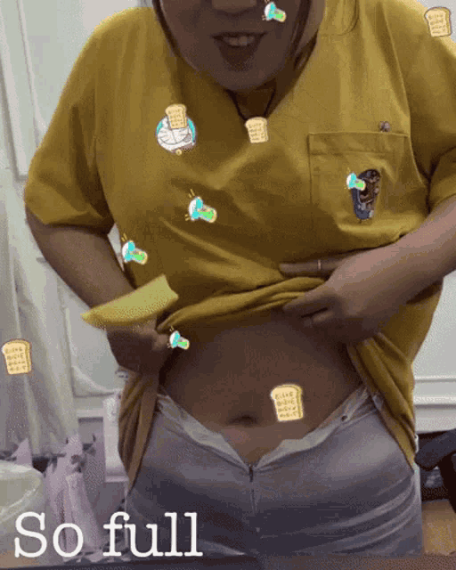 a woman in a yellow shirt has stickers on her stomach including one that says ' so full '