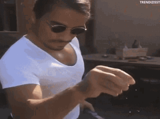 a man wearing sunglasses and a white shirt is holding something in his hands .