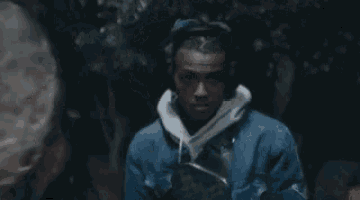 a man wearing headphones and a denim jacket is standing in a dark room .