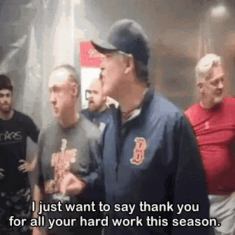 a man in a boston red sox jacket is talking to another man in a baseball cap .