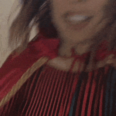 a woman in a red and black striped shirt is smiling and holding a piece of pizza .