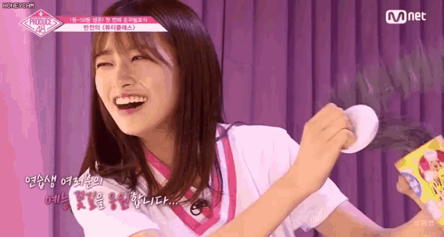 a girl is holding a cotton ball in her hand and smiling while wearing a pink shirt .