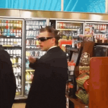 a man wearing sunglasses stands in front of a shelf that says sweetz