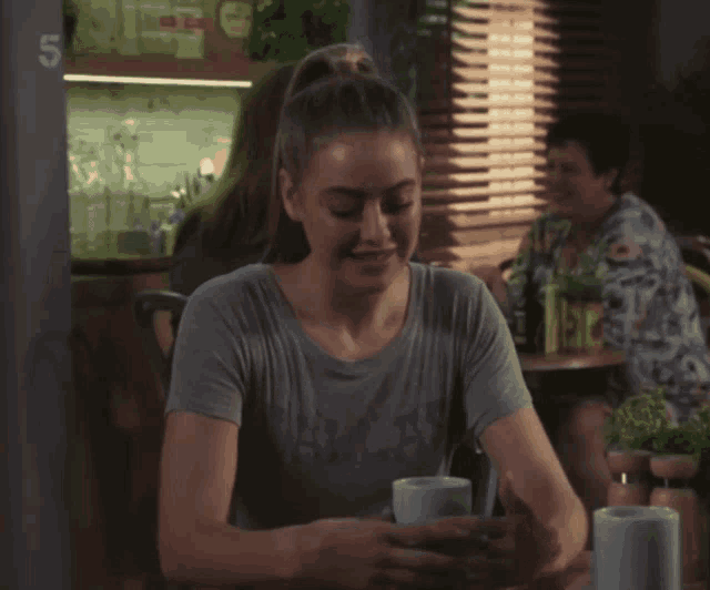 a woman wearing a dallas shirt sits at a table with two cups of coffee