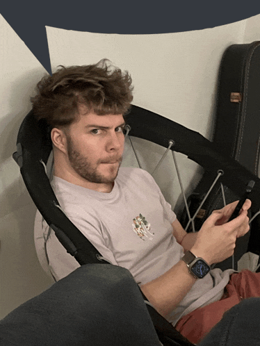 a man with a beard is sitting in a chair looking at his phone