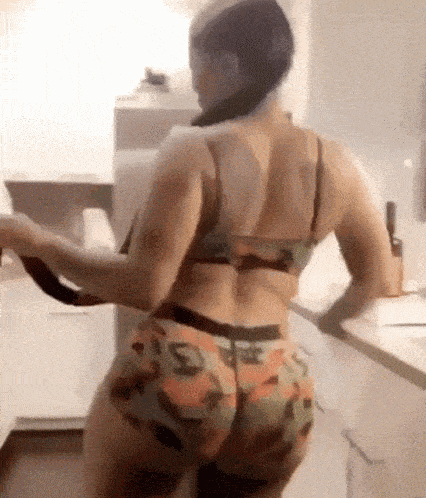 a woman in a bikini is standing in a kitchen holding a spoon .