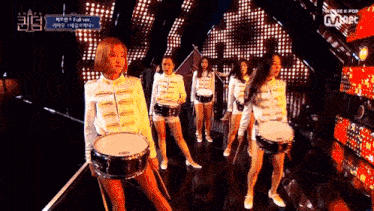 a group of young women are playing drums on a stage with a mnet logo in the background