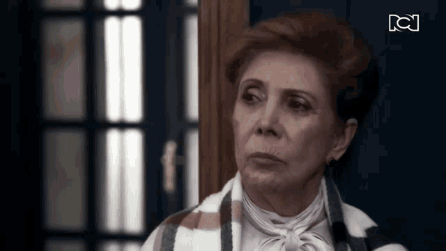 an elderly woman is standing in front of a door looking at the camera .