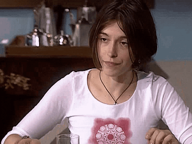 a woman in a white shirt is sitting at a table with a glass of water .