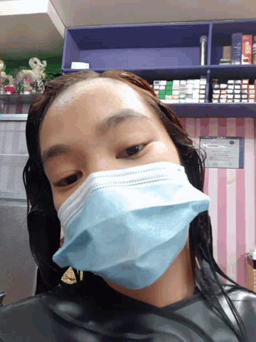 a woman wearing a blue face mask stands in front of a pink and purple wall