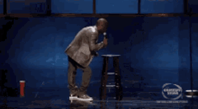 a man in a white coat is dancing on a stage in front of a window .