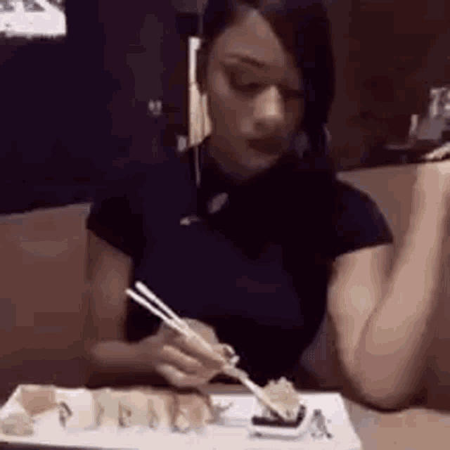 a woman is eating sushi with chopsticks from a plate .