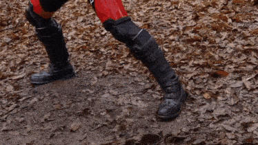 a person wearing black boots and red pants is walking on a path covered in leaves