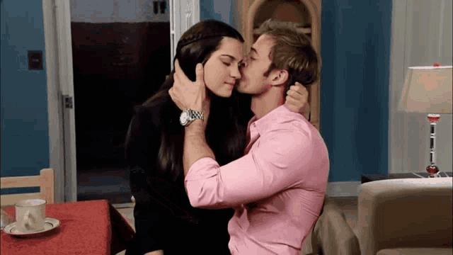 a man in a pink shirt is kissing a woman on the cheek