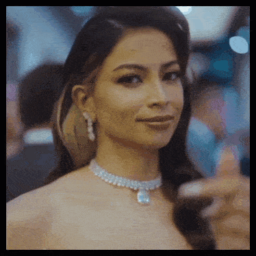 a woman wearing a necklace and earrings is smiling and giving a thumbs up