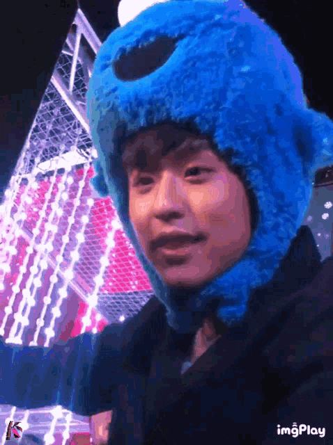 a person wearing a blue cookie monster hat is standing in front of a christmas tree