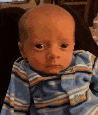 a baby is wearing a blue and yellow striped shirt and looking at the camera