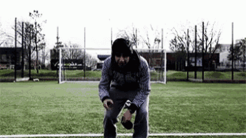 a man is squatting on a soccer field holding a bottle of beer .