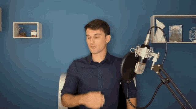 a man in a blue shirt stands in front of a microphone with the letter a on it
