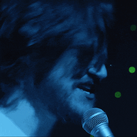 a man wearing sunglasses is singing into a microphone with his mouth open