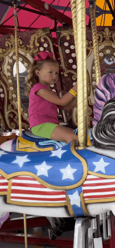 a little girl is sitting on a merry go round