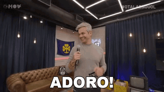 a man is holding a microphone in front of a couch and the word adoro is above him